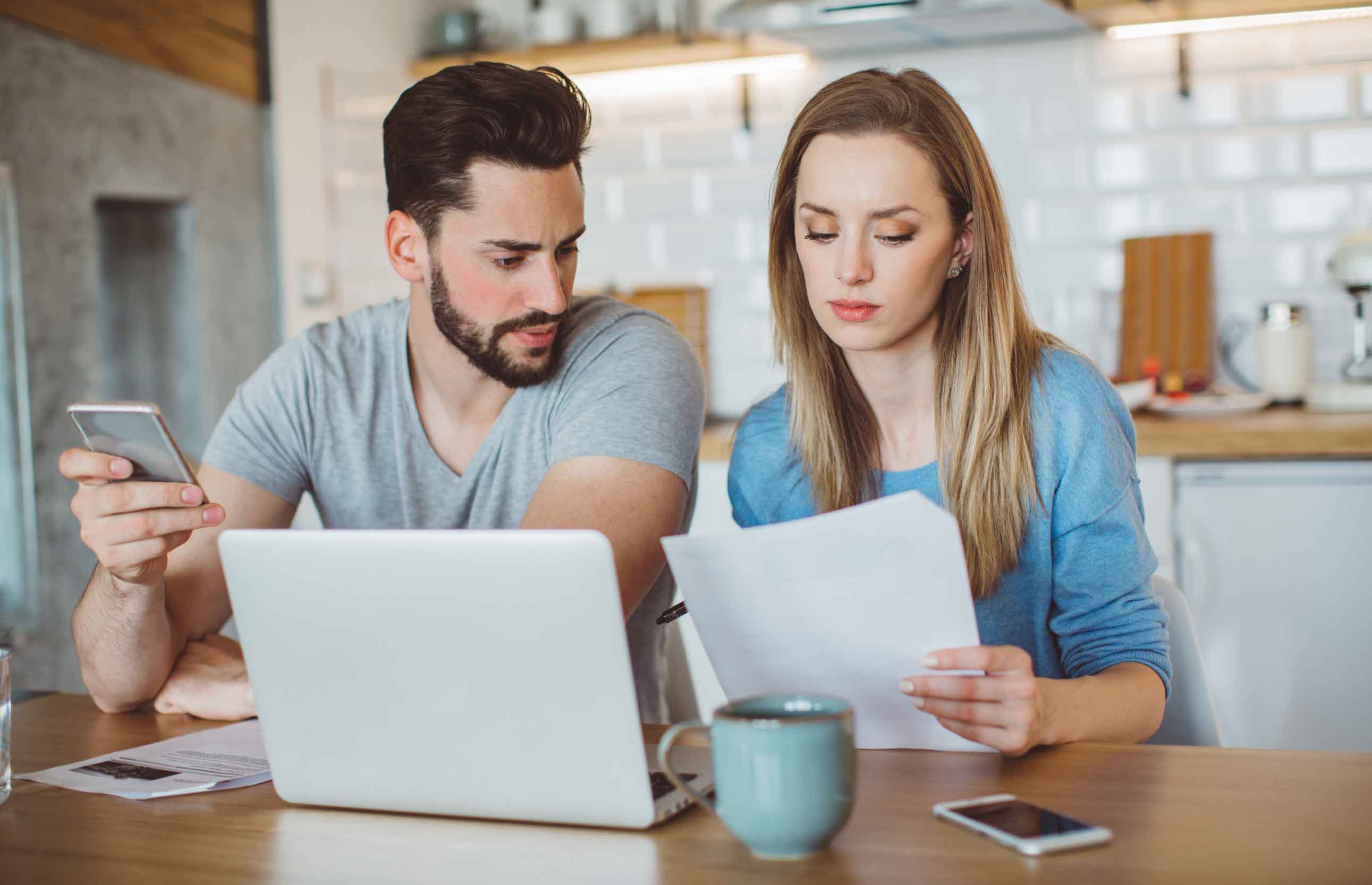 A young white couple sit at a kitchen table on a laptop reviewing their tax filing for 2021