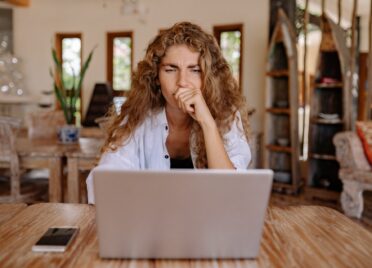 A woman looks at her laptop computer with a thoughtful look on her face.