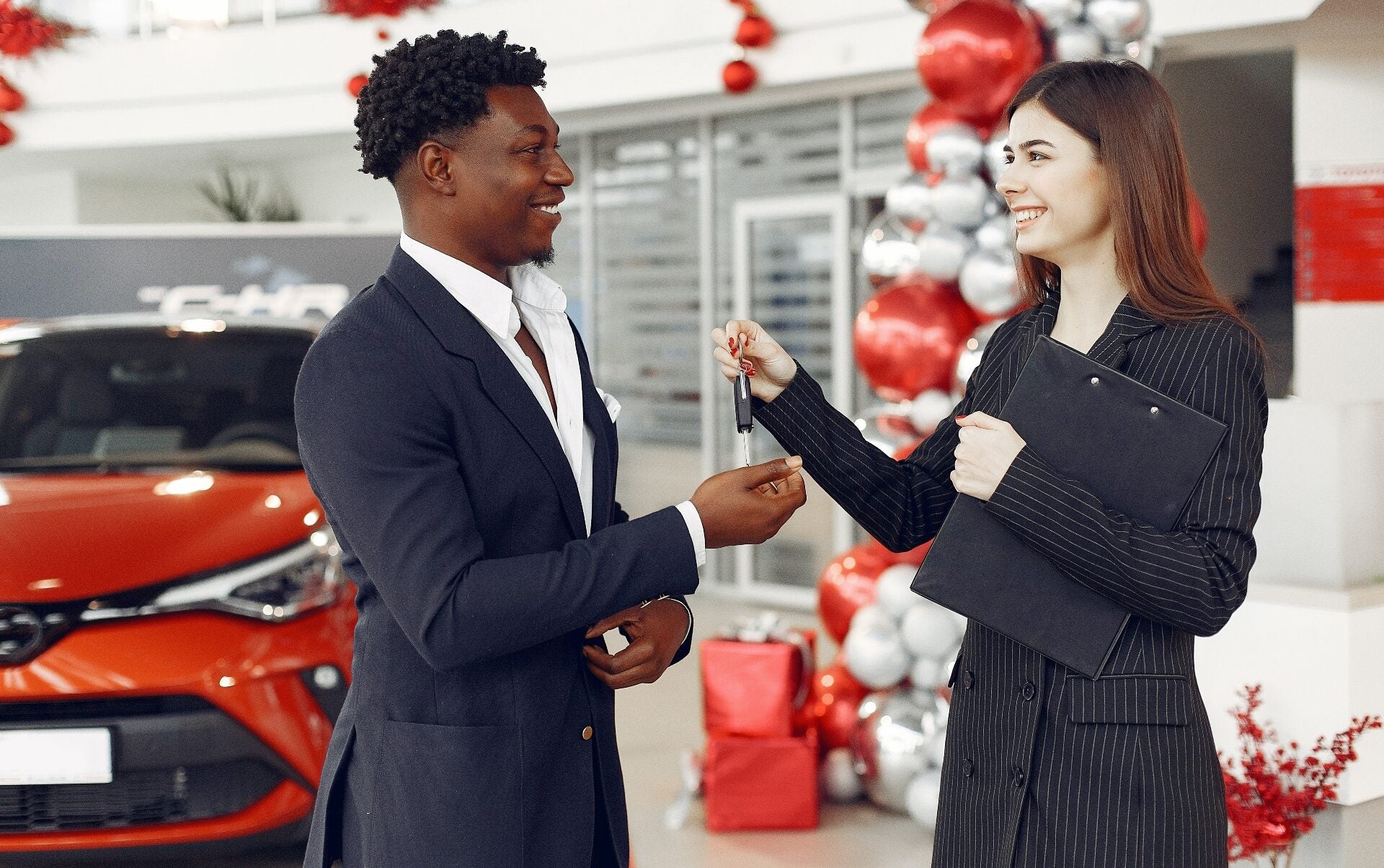 A smiling woman hands a man the keys to a car he just successfully leased