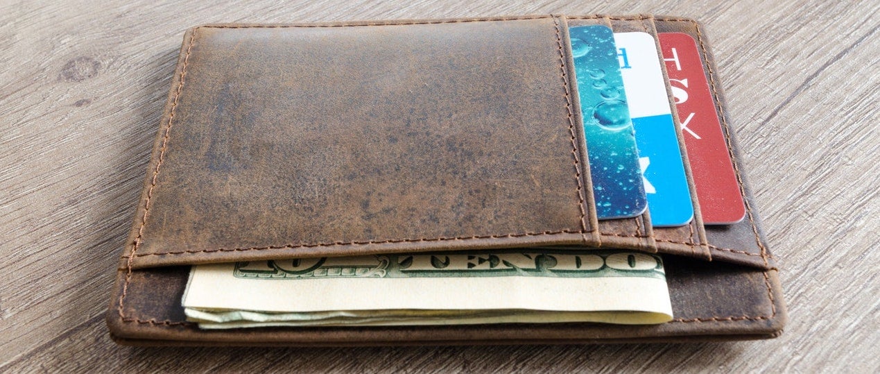 A closeup of a brown wallet with various cards and dollar bills
