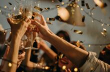 A close up of people holding wine glasses in celebration as gold confetti falls.