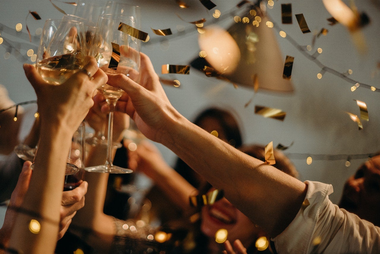 A close up of people holding wine glasses in celebration as gold confetti falls.