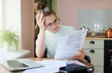 A young woman looks at health insurance paperwork with frustration and confusion