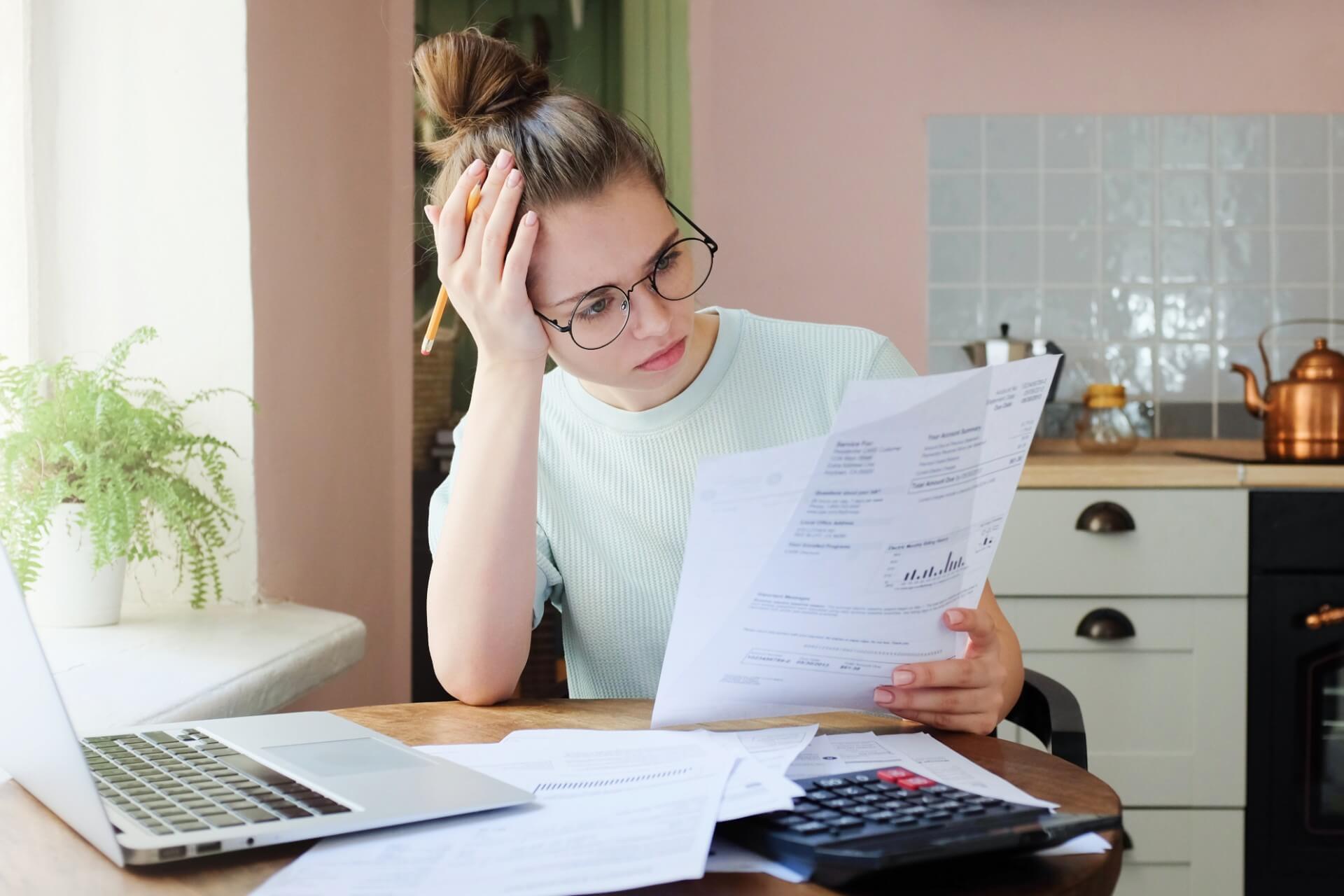 A young woman looks at health insurance paperwork with frustration and confusion