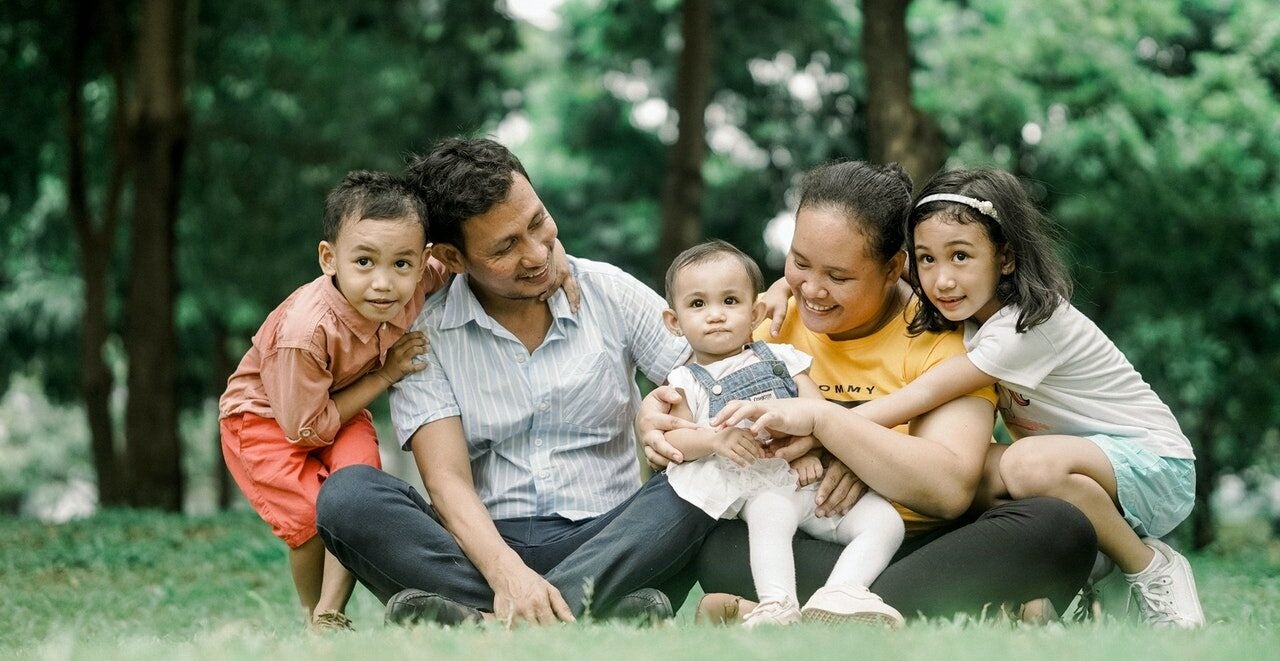 A young family embraces while sitting on the grass outside and learning to build a financially secure future.