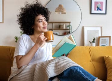 A woman enjoys coffee and a book in her new home.