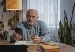 An Elderly Man Using His Mobile Phone while Holding a Credit Card