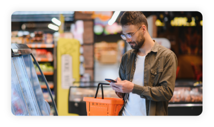 Quick text during shopping. Handsome young man holding mobile phone and smiling while standing in a food store