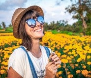 A smiling woman stands in a field of yellow flowers after learning how to reduce debt.