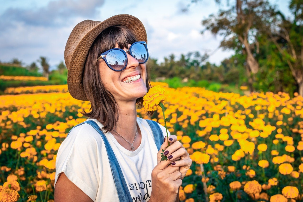 A smiling woman stands in a field of yellow flowers after learning how to reduce debt.