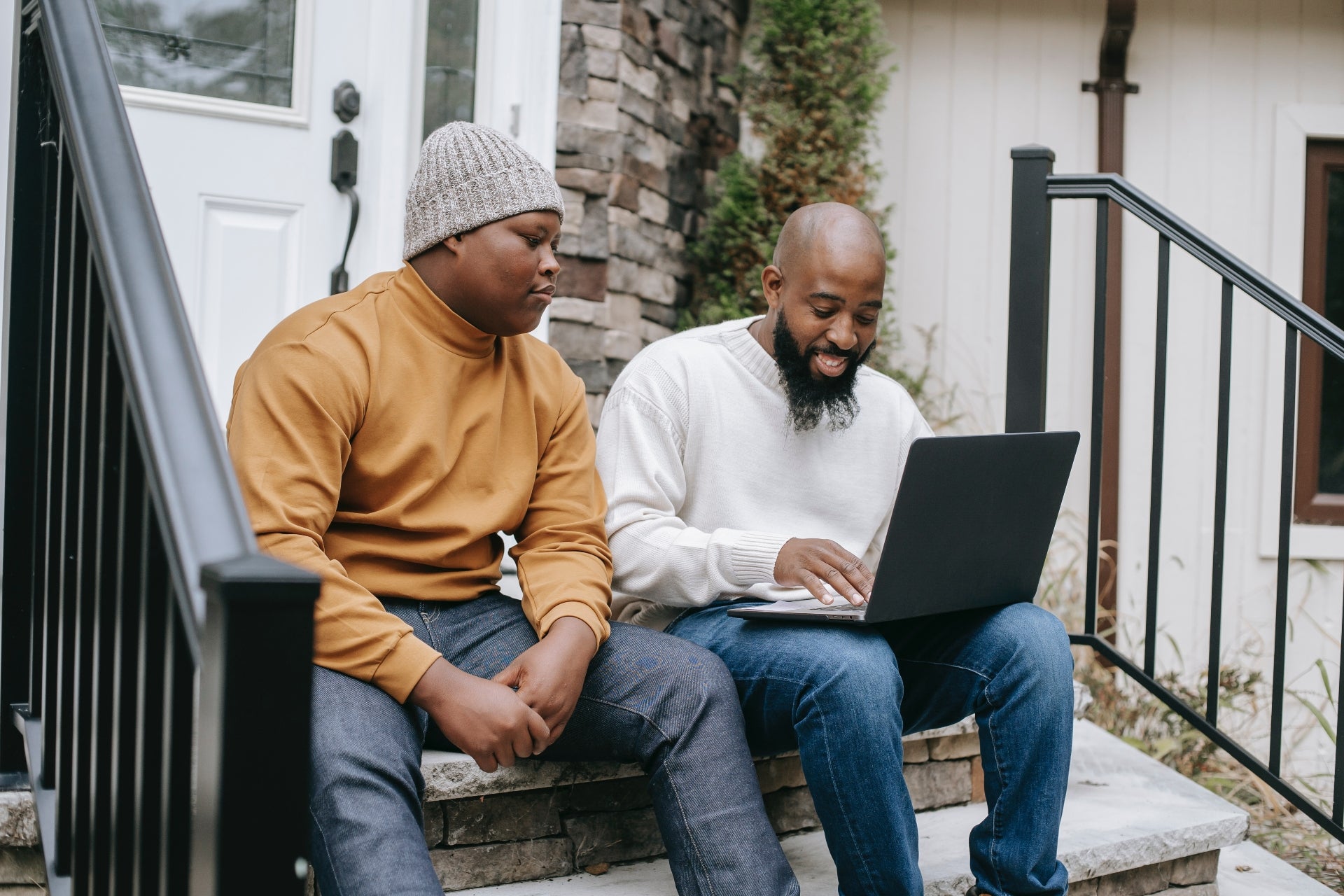 A father and son sit on a porch looking at the father's laptop to learn more about credit age