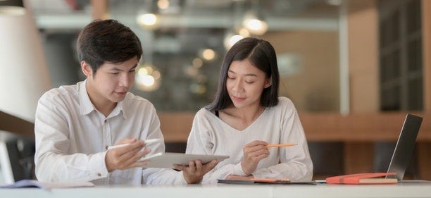 A man and a woman sit a table, looking on a tablet and discussing how to take control of finances.