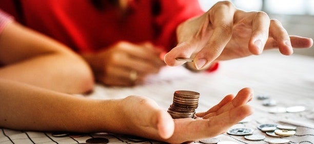 a stack of coins sits in a person's hand. Another person is taking a coin off the stack. 