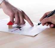 woman's hand pointing to paper work to show man holding pen how a mortgage works