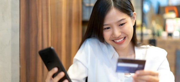 Asian woman holding phone and credit card while searching for what is a credit card on the phone