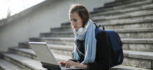 A student sits on steps while working on her laptop.