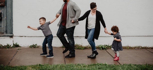 A young family holds hands walking down a sidewalk.