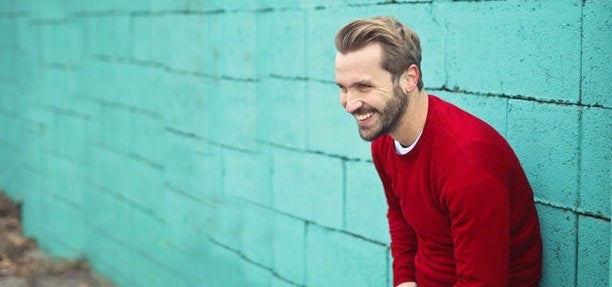 A man in a read shirt leans against a wall, laughing.