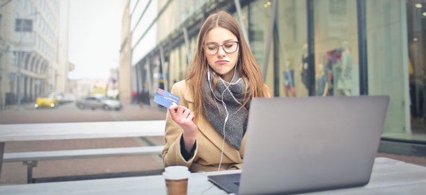 A woman sits with her laptop in front of her, while holding a credit card.