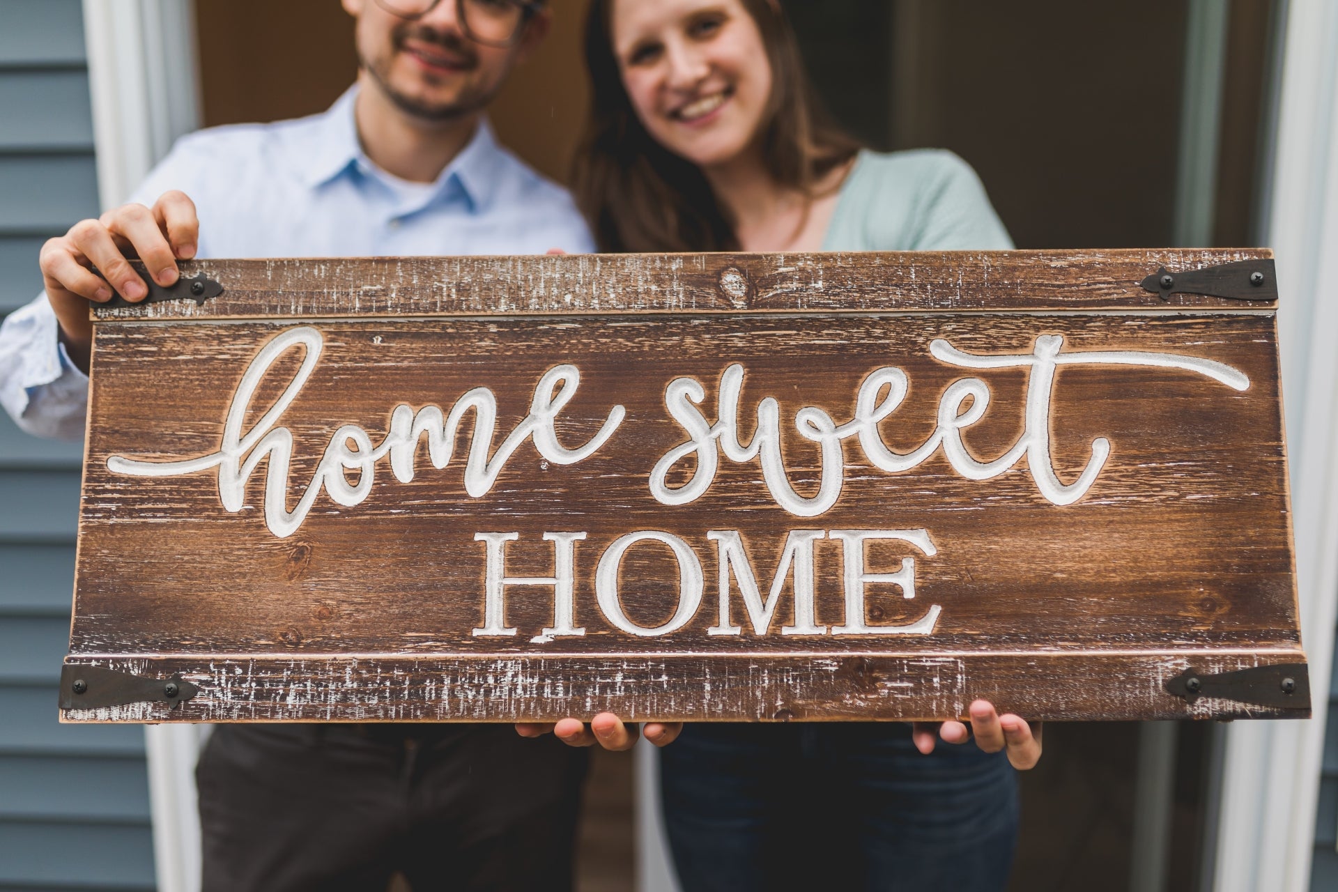 A young couple holds a wooden sign that says Home Sweet Home