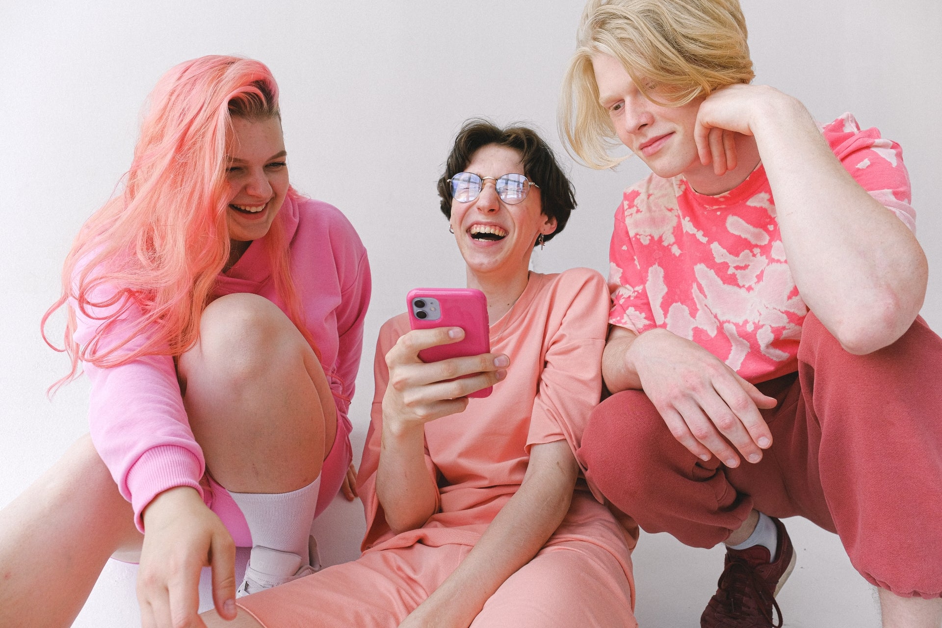 Three young people wearing pink laugh and look at a cell phone